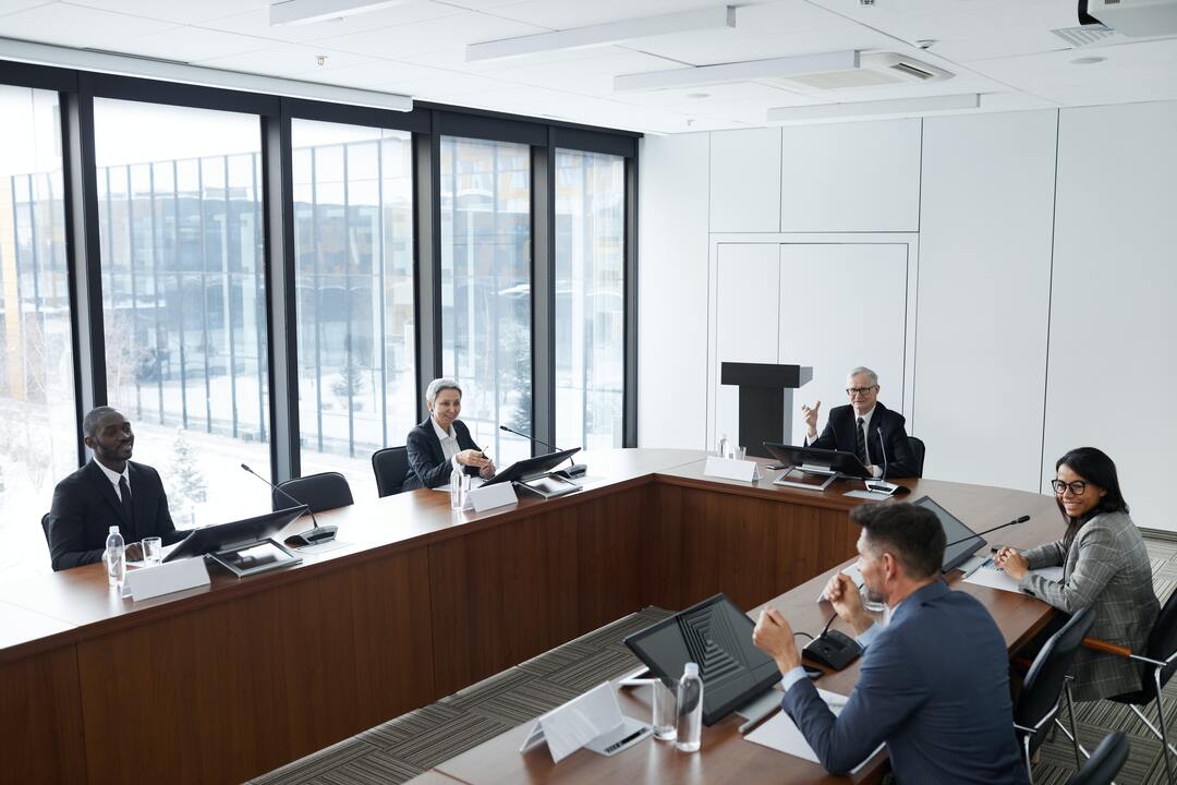 Organizational behavior: na imagem é possível ver uma sala de reuniões na qual tem uma mesa de madeira em formato de "U" e pessoas sentadas nas cadeiras.